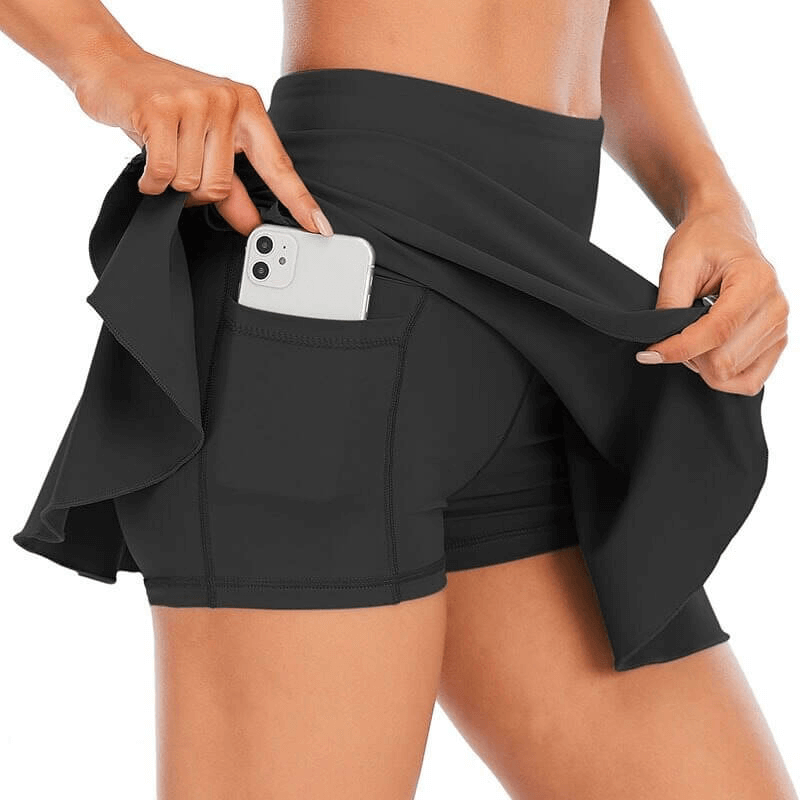 Woman wearing high waist tennis skirt-shorts with pocket holding a phone, emphasizing comfort and functionality for active wear.